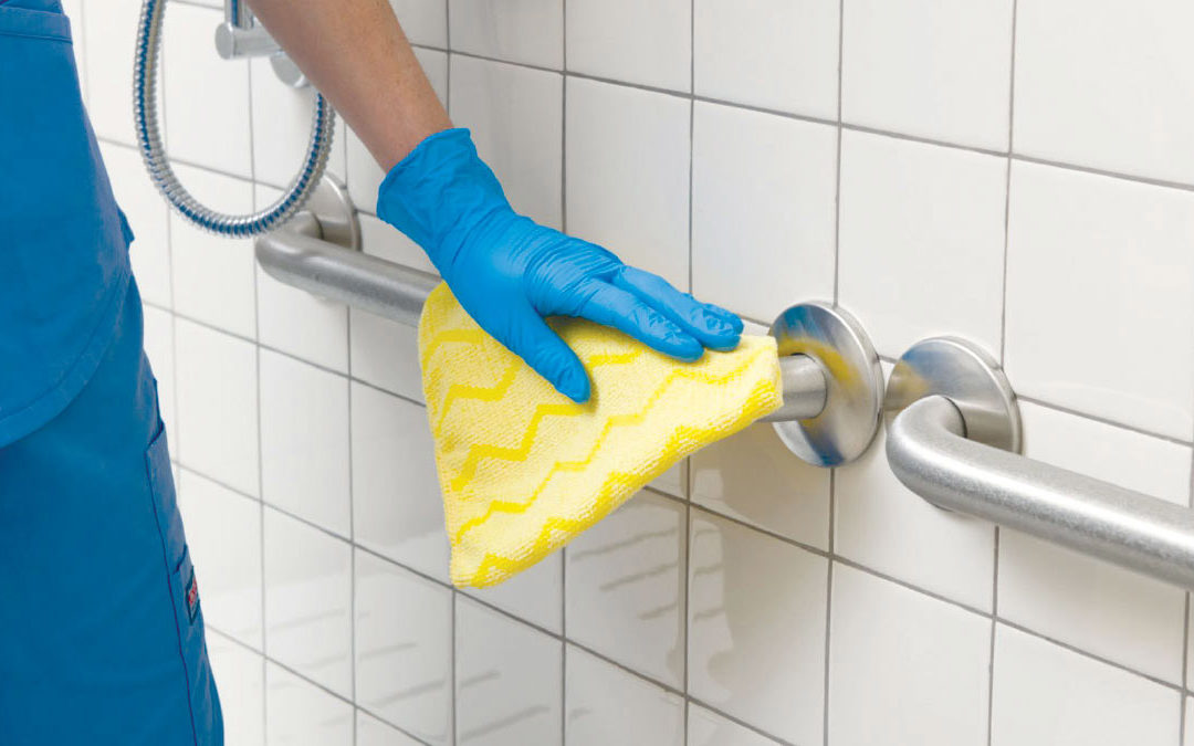Gloved Hand Wiping Down Grab Bars in Bathroom with Yellow Rag